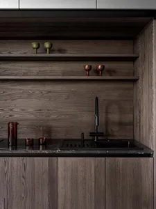 Modern kitchen with wooden cabinets, a black sink, and a wooden countertop, featuring a shelf with glasses and a dimly lit atmosphere