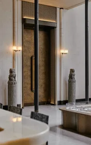 A well-lit, modern lobby with marble and stone surfaces, featuring a variety of furniture and sculptures, and a warm, inviting atmosphere