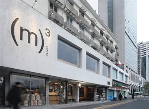 A modern coffee shop with a white exterior and a large window, surrounded by tall city buildings, offering a welcoming atmosphere with natural light
