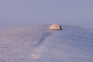 A serene snowy landscape with a small white dome-shaped hut standing out against the white background