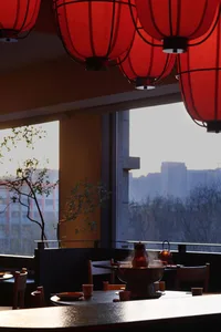 Dining area with a table, chairs, and red accents, set with a bowl and a vase, in a modern restaurant with natural lighting and a warm color palette