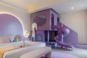 A dimly lit purple child's bedroom with a bed, slide, chair, and potted plant, creating a cozy and inviting atmosphere