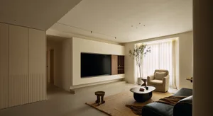 Cozy modern living space with a flat screen TV, a couch, a chair, a coffee table, and a potted plant, lit by natural and artificial light