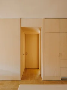 A calm and inviting bedroom with a white room, a brown door, and a tile floor, lit by natural light from the open doorway to the hallway