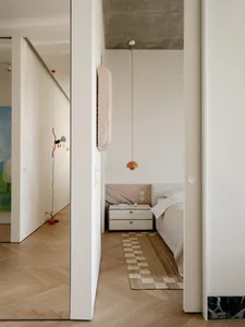 A small white bedroom with a bed positioned under a mirror, a dresser, and a calm atmosphere