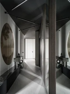 A modern hallway with a wooden floor, stone countertop, and a white door, decorated with framed pictures and a mirrored wall in a dimly lit space