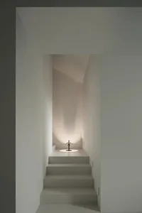 A dimly lit narrow hallway with a staircase made of concrete and a light in the corner, casting a warm glow