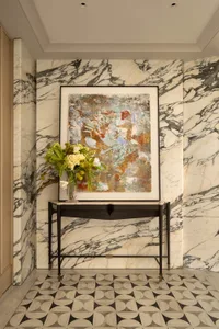 A modern living space with a black frame around a painting of a marble wall, a vase with flowers, and a black bench in the center of the room