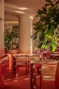A modern restaurant interior with red tablecloths, red chairs, and large pillars, set in a well-lit dining area