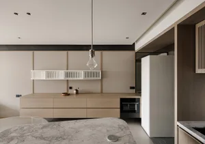 A modern kitchen with a large island featuring a brown marble countertop, well-lit with a sink on the right and a refrigerator in the background