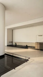 Modern living space with a white color scheme, a large fireplace, a sink, and a counter, with natural light from a large window