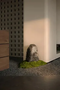 A serene room with a rock on a bed of moss, surrounded by a white wall and a wooden cabinet, on a gravel surface