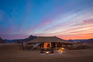 Desert-style house with a geodesic dome structure, surrounded by sandy landscape and mountains, featuring a modern and minimalistic interior with open spaces and natural materials