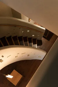 A spiral staircase in a dimly lit museum with a white and brown color scheme, featuring a wooden staircase and metal railing