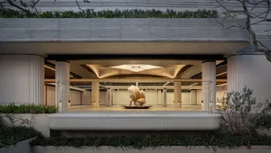 A dimly lit, modern building lobby with a large metal sculpture as the centerpiece, surrounded by concrete walls and floors