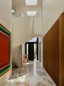 A modern house with a white and wood-paneled interior, featuring a spiral staircase with a white railing and a large window, bathed in natural light
