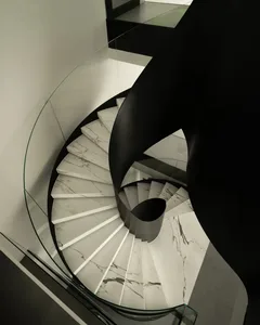 A black and white photograph of a spiral marble staircase in a room with a glass wall, surrounded by elegant decor and natural light