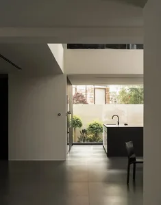 A modern kitchen with a white color scheme, featuring a sink, dining table, and chair, with natural light from a window creating a warm atmosphere