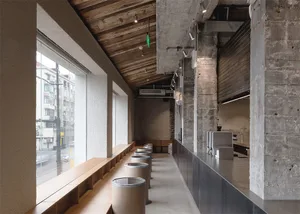 A spacious dining room with a high ceiling, wooden floor, and tables and chairs, lit by dim overhead lighting