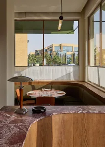 Dining area with a table, chairs, and couch, set with wine glasses, cups, and bowls, surrounded by wood and marble, near a window with natural light
