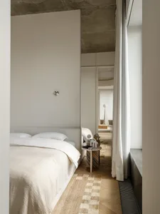 A well-lit bedroom with a bed, a mirror, and a table, surrounded by white walls and wood accents