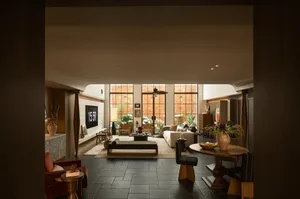 A modern living dining kitchen space with a couch, dining table, chairs, sink, refrigerator, and potted plants, decorated with vases and a bowl, under warm and inviting lighting