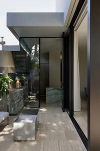 Well-lit bathroom with a large window, marble surfaces, and glass accents, featuring a sink, toilet, and shower
