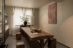 Rustic dining room with a wooden table, chairs, and books, lit by natural light from a window