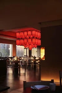 A warm and inviting restaurant dining area with a large red and white chandelier, multiple chairs and tables, and natural light from the windows
