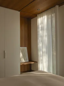 A calm and inviting bedroom with a white bed, a wooden dresser, and natural light from a window