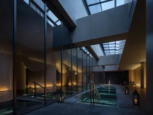 A large, modern building with a glass-walled pool area, surrounded by natural light and luxurious materials