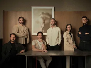 A group of people posing together in a casual gathering space with a dining table at its center, surrounded by natural and artificial lighting