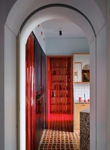 A modern kitchen with a red door and wall, featuring a counter with a sink and refrigerator, and dim lighting creating a cozy atmosphere