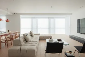 A well-lit living room with a white couch, a black chair, a wooden floor, and a dining table and chairs, creating a comfortable and inviting atmosphere