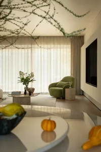 A modern living room with a green chair, dining table, and TV, featuring a large window for natural light and a variety of materials including wood and glass, creating a comfortable and inviting atmosphere