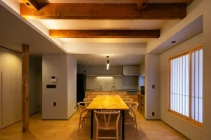 A modern kitchen and dining area with a wooden table, chairs, and various appliances, illuminated by natural light