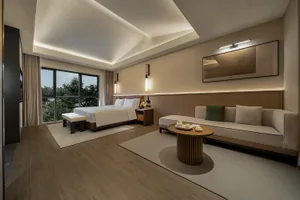 A well-lit bedroom with a wooden floor, a bed near a large window, and a couch in the opposite corner, creating a cozy atmosphere