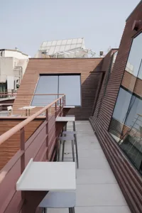Photograph of a modern building with a brick facade, large window, and balcony, featuring a comfortable and inviting interior with chairs and dining tables