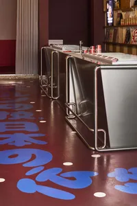 Modern kitchen dining space with blue floor, red wall, metal sinks, and wooden dining table, well-lit and inviting