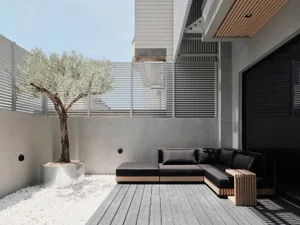 A well-maintained outdoor living space with a black couch, a brown chair, and a tree in the background, surrounded by a fence