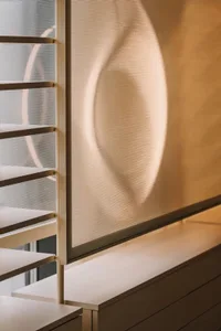 A room with a white wall and a window with a mesh shade drawn down, allowing natural light to filter in