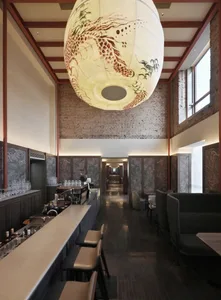 A modern restaurant with a bar and dining area, featuring a large open layout, high ceilings, and natural light, with artwork on the walls and various furniture and decorative elements