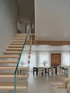 A modern living room with a staircase, dining table, couch, and sink, decorated with various items, featuring a warm and inviting atmosphere with natural lighting