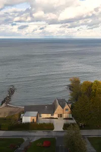 A modern beach house with a large window on the second floor, surrounded by trees and natural scenery, bathed in natural light