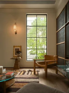 A modern living room with a chair near a large window, a couch in the center, and a television on the right, featuring a combination of wood and glass elements and natural lighting