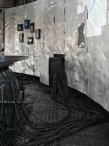 A cluttered workspace with a black table surrounded by wires, likely used for electronics or devices, in a room with a somewhat busy and industrial appearance