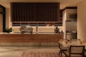 Cozy restaurant interior with a brick wall, bar, and dining area, featuring a counter with a coffee maker and blender, and a dining table with chairs