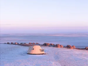 A serene snow-covered field with a cluster of small, round, white structures, possibly serving as shelters or architectural features