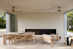 Cozy living room with a wooden floor, white walls, a dining table, chairs, a couch, and a fireplace, lit by natural sunlight