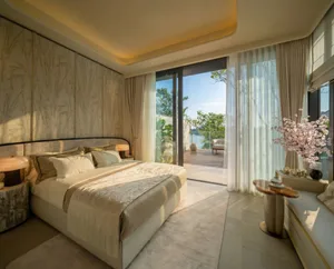 A well-lit bedroom with a bed, chair, and window, featuring white furniture and a clean, organized appearance